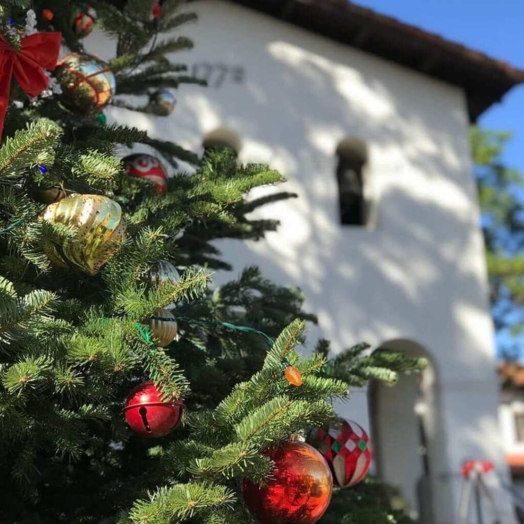 A decorated Christmas tree in front of the Mission San Luis Obispo de Tolosa in the daytime.