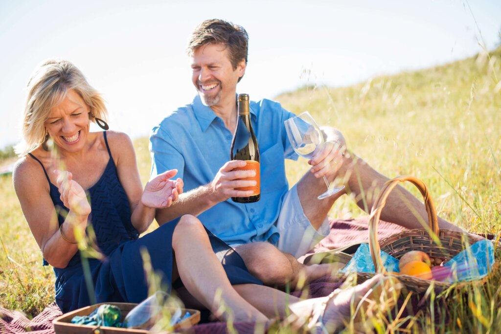 Photo of man and woman enjoying a bottle of wine on a grass field.