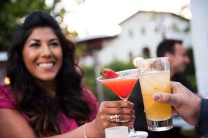 Woman holding up a cocktail and doing a toast with a friend. 