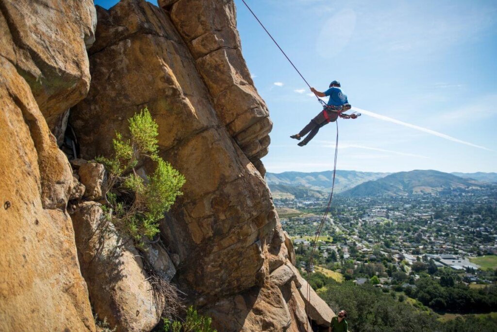 A climber belaying down the stone face of a mountain in San Luis Obispo