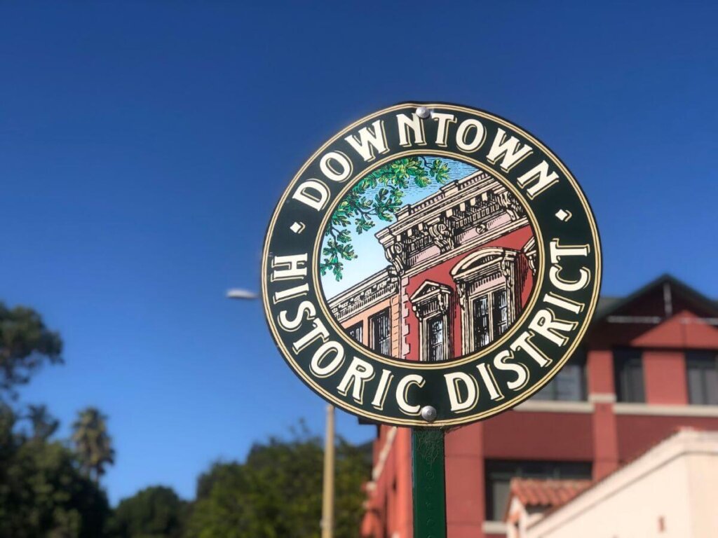 The round Downtown Historic District street sign in front of a brick building and blue sky in San Luis Obispo, California.