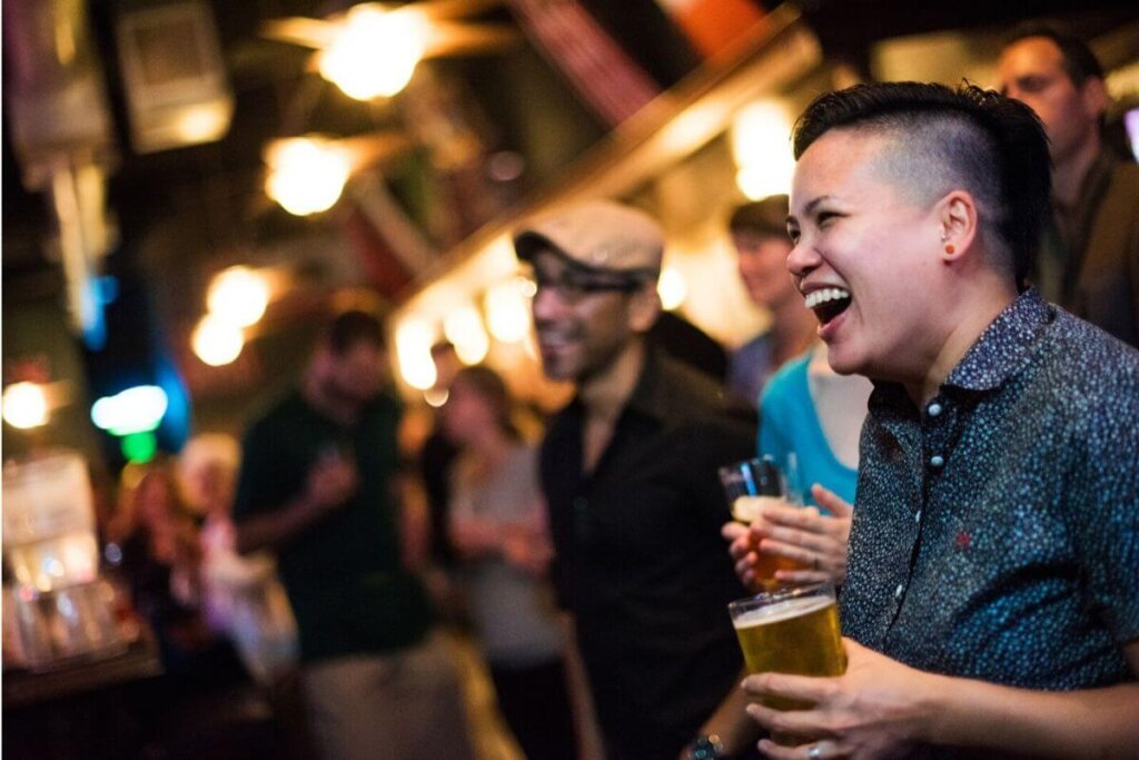 Laughing people in a dim bar, holding pints of beer in hand.