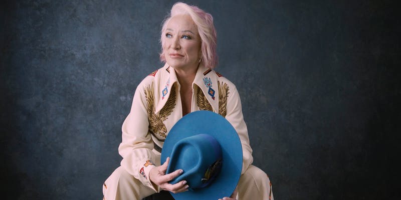 Tanya Tucker with a country-western suit and a blue cowboy hat in hand.