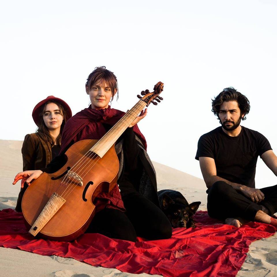 Arthur Watership and 2 other bandmates with a cello on a red blanket at the sand dunes.