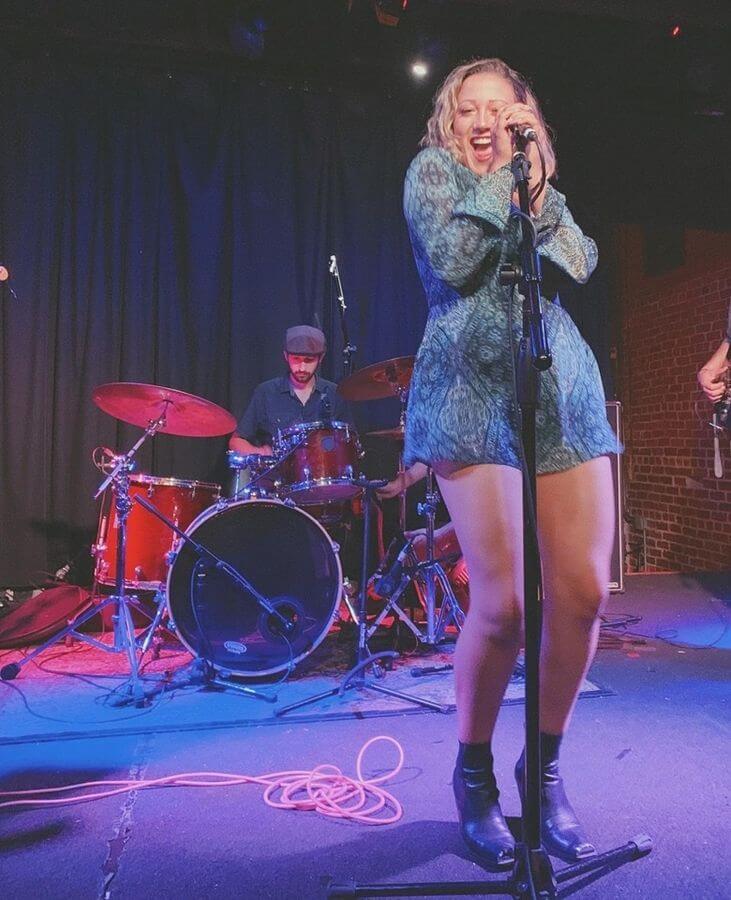 Lauren Hall singing on stage in front of the drummer in the colored stage lights.