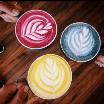 Overlooking shot of 3 lattes, one blue, one red, and one yellow from Kin SLO Coffee Shop.