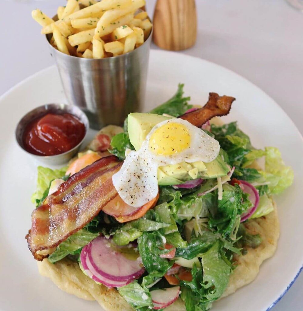 French fries in an open tin on a plate with a salad, topped with bacon and a fried egg from Piadina in San Luis Obispo.