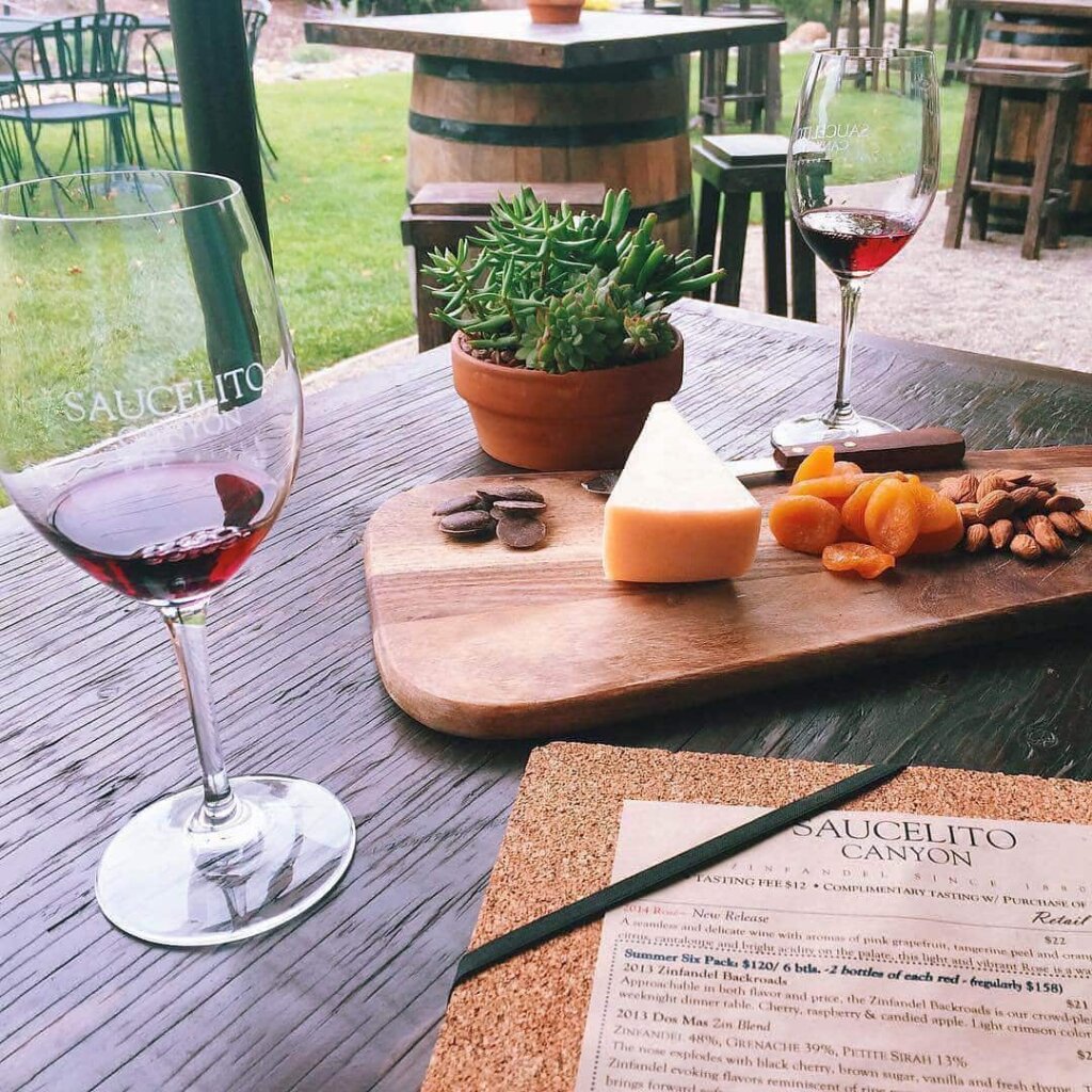 2 glasses of red wine with cheese and a menu at Saucelito Canyon Vineyard.
