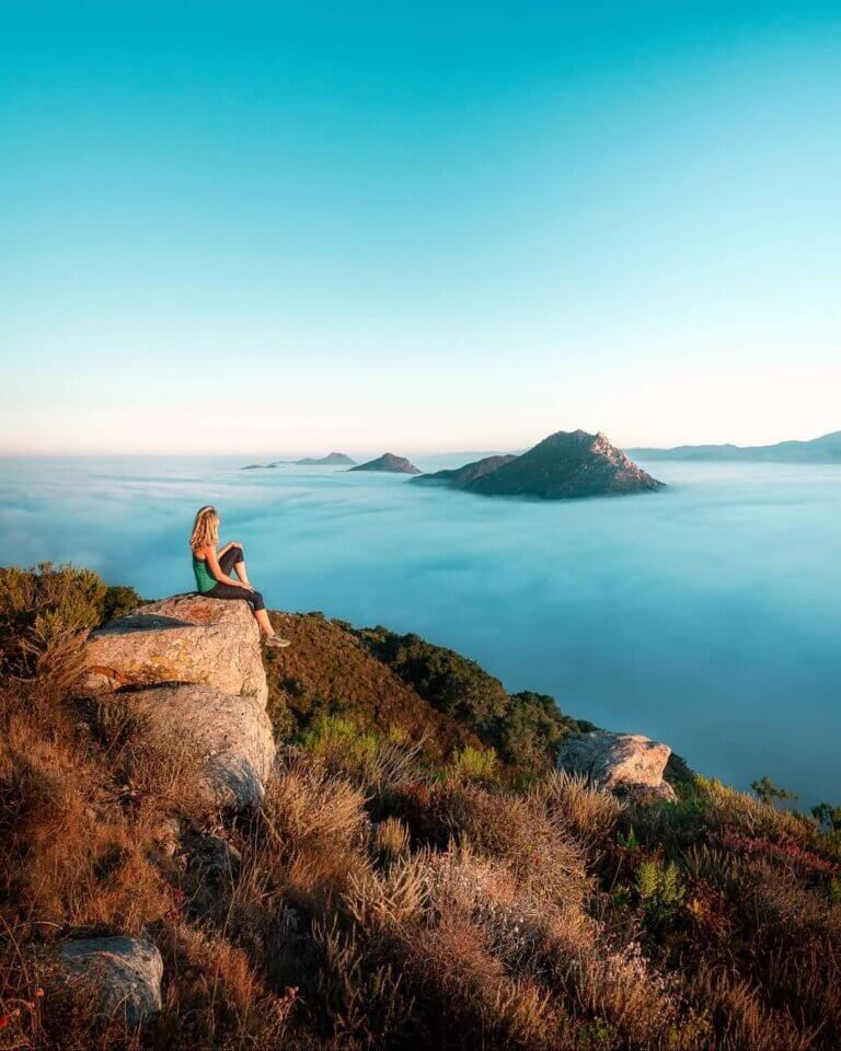 woman sitting on a hill overlooking a scenic view